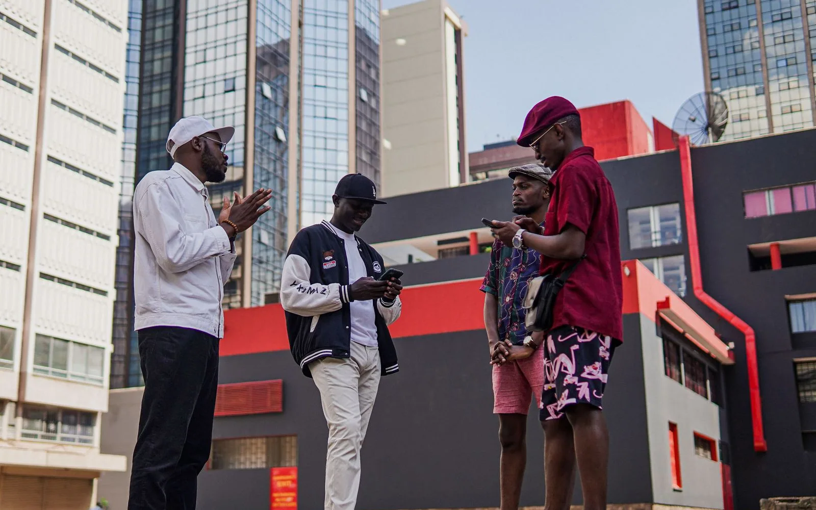 Four young men looking at their phones on a city street among office towers