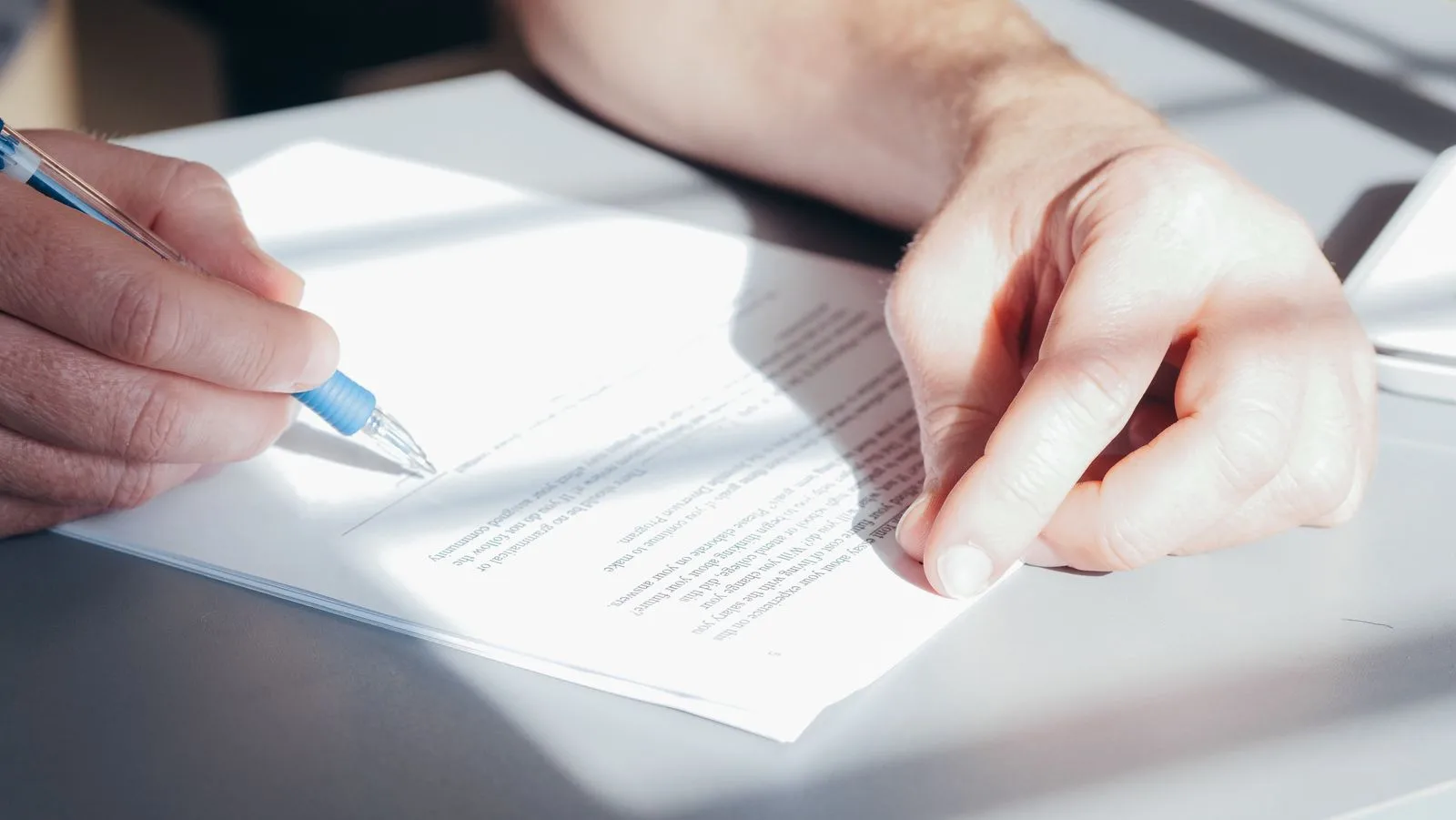A hand signing a document with a blue pen